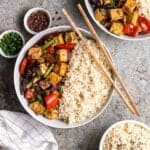 Bowl of rice and szechuan tofu served with chopsticks with green onion, peppercorn and bowl of rice beside.