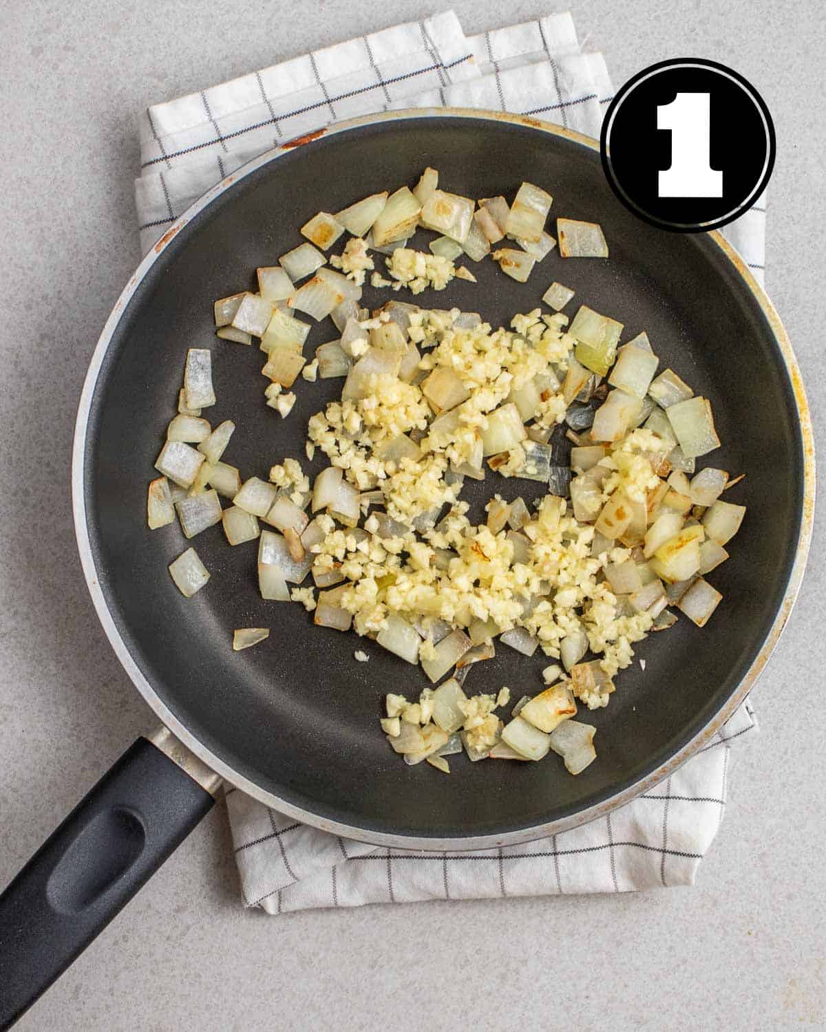 Sauteed onion and garlic in a non-stick pan on a folded white teacloth.