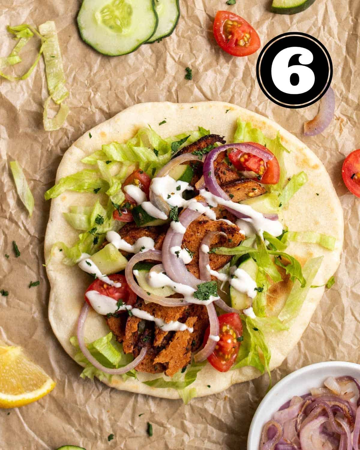 Seitan doner wrap on a wax paper with caramelized onion beside.
