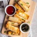 Tofu egg rolls on a chopping board served with ketchup and soy sauce.