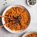 Plate of gochujang fried rice topped with nori sheets served with chopsticks.