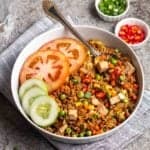 Nasi goreng with cucumber and tomato slices beside served with a spoon.
