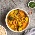 A bowl of Jamaican curry served with spoon with bowl of rice and chopped cilantro beside.