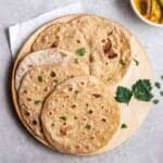 4 vegan roti on a wooden board topped with cilantro with bowl of curry beside.