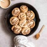A pan of cinnamon rolls with spoonful of cinnamon powder and icing beside.