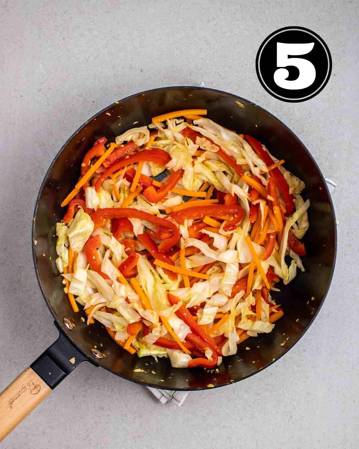 Cooked bell pepper, cabbage, and carrot in a wok.
