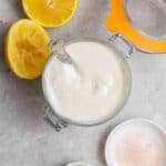 A jar of silken tofu mayo with spoon with lemon halves and salt beside.