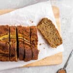A partially sliced loaf of banana bread on a wooden board lined with parchment paper.