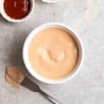 Bowl of vegan sriracha mayo with butter knife and sriracha beside.