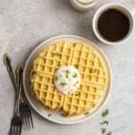 A plate of chickpea flour waffles with forks, coffee, and a jar of mayo beside.