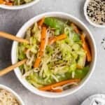 Yasai itame served with chopsticks with sesame seeds and rice beside.