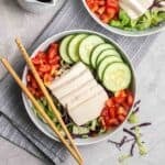 A bowl of cold tofu salad served with chopsticks on a black and white striped teacloth.