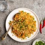 A plate of tom yum fried rice served with spoon with chilies, green onion and water beside.