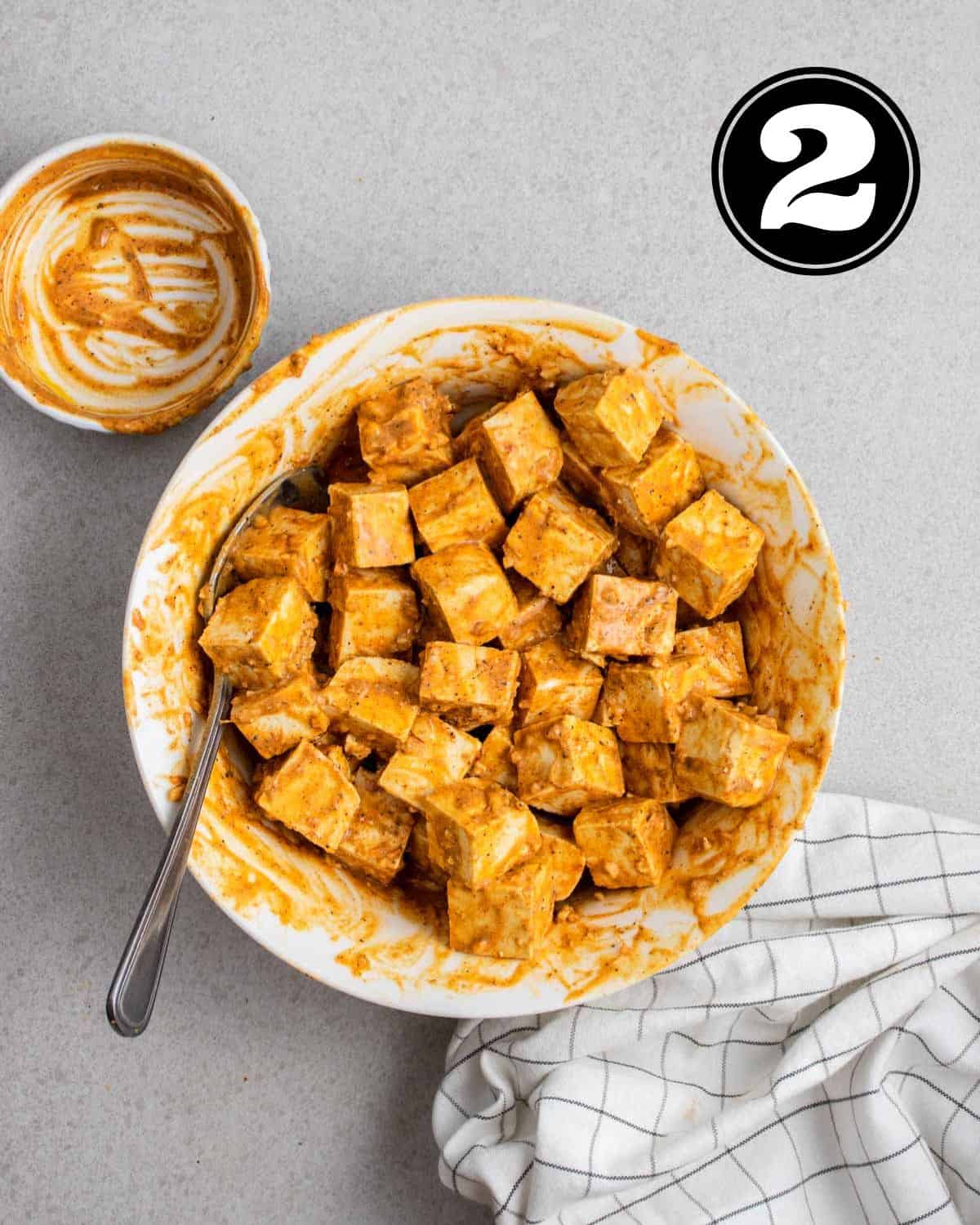 Marinating tofu cubes in tandoori sauce in a large bowl with a spoon beside.