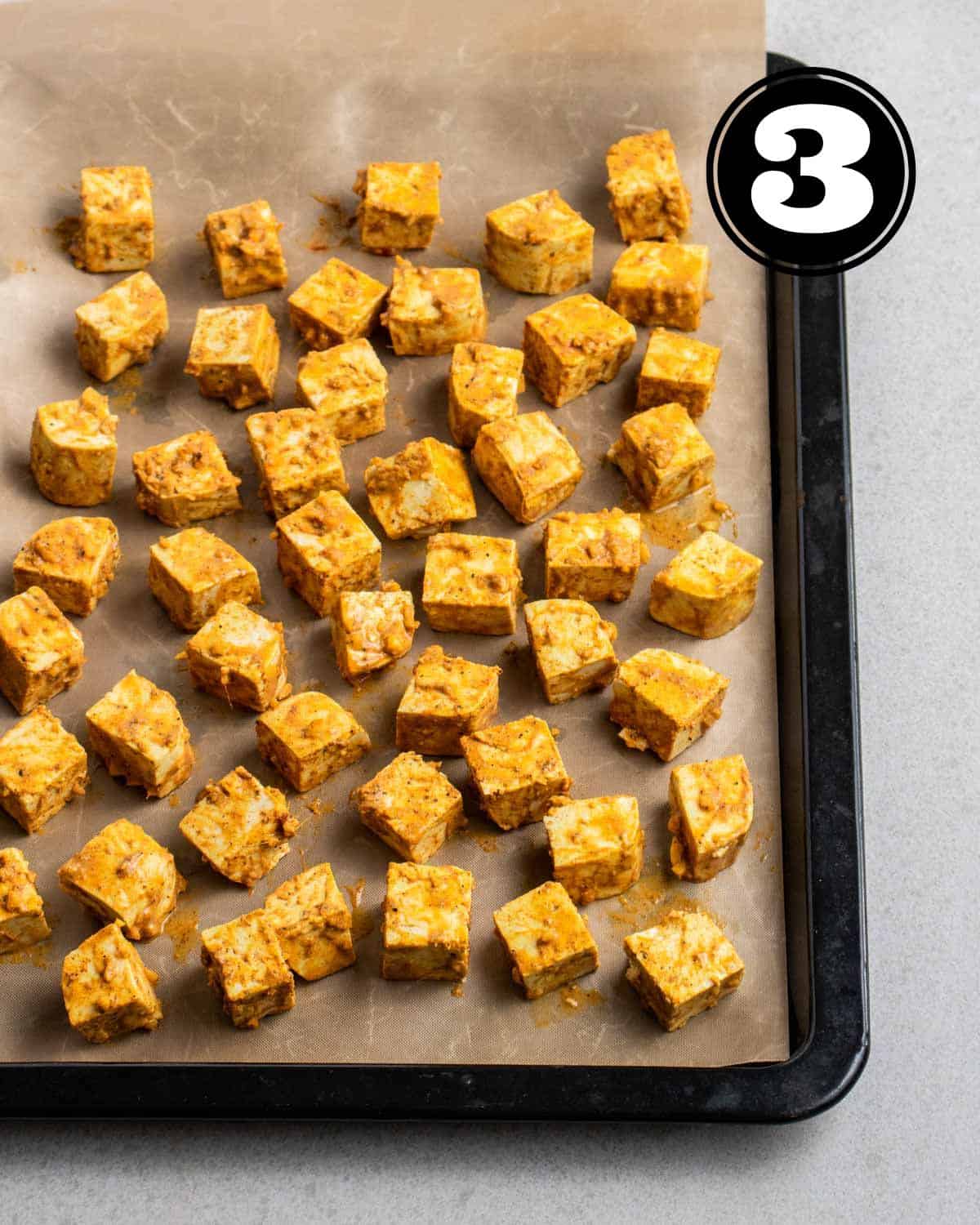 Unbaked tandoori tofu cubes on a baking tray lined with parchment paper.