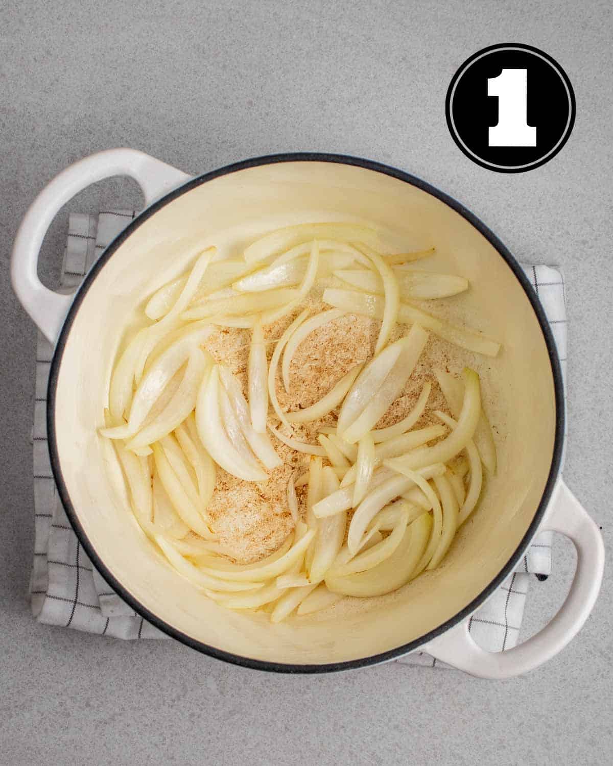 Cooked onion in a white Dutch oven on a white checkered folded teacloth.