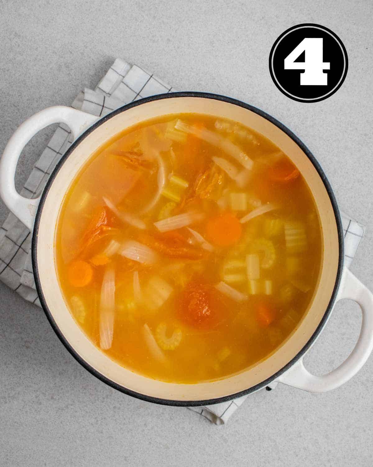 A pot of ABC soup in a white Dutch oven on a white folded teacloth.