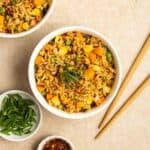 2 bowls of vegetable Thai fried rice with chopsticks, green onion, and chili flakes beside.
