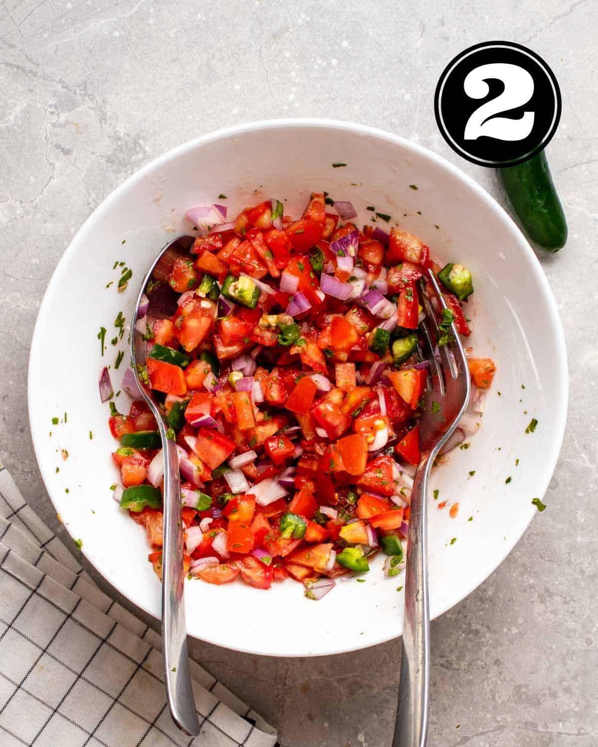 A bowl of salsa with a spoon and fork beside.