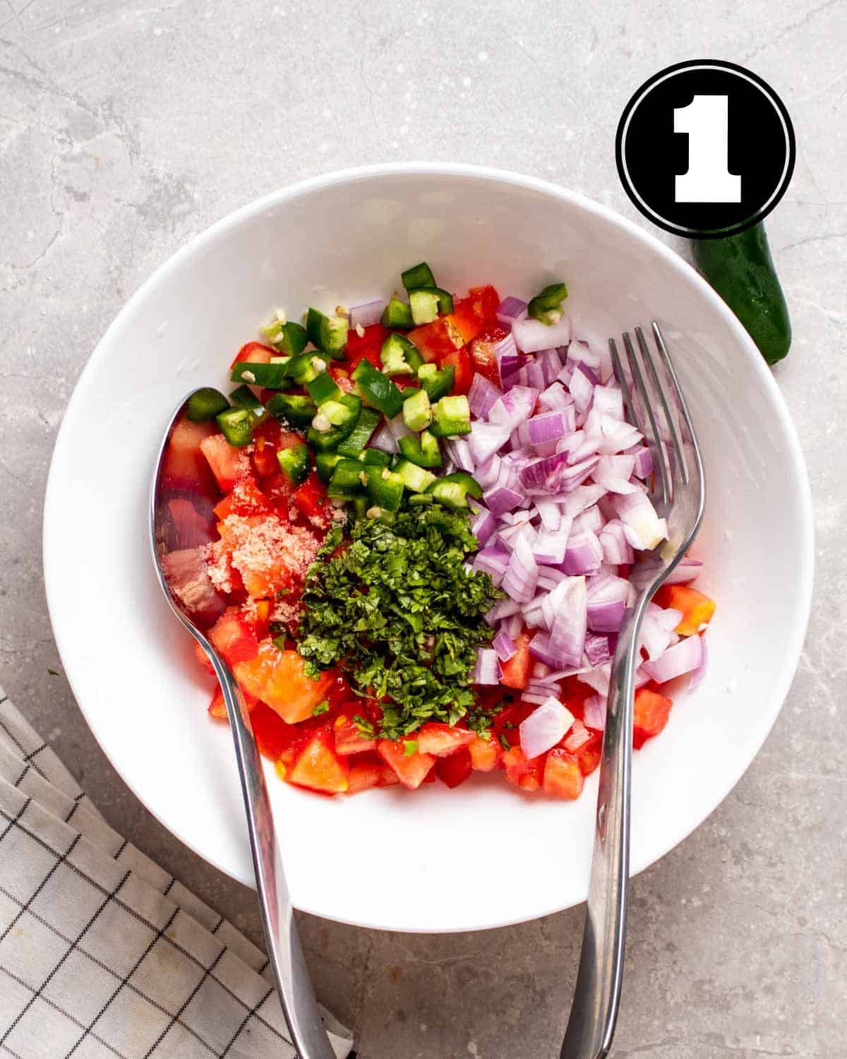 Chopped ingredients for salsa in a bowl with a spoon and fork beside.