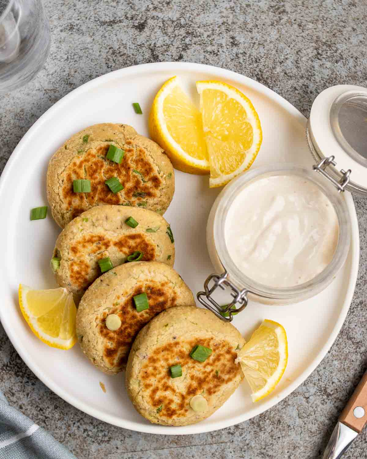 Chickpea patties arranged on a plate served with lemon wedges and vegan yogurt.