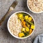 Thai yellow curry served with rice in a white bowl with bowl of rice and a fork beside.