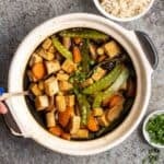Spooning out some braised tofu from a claypot with rice and green onion beside.
