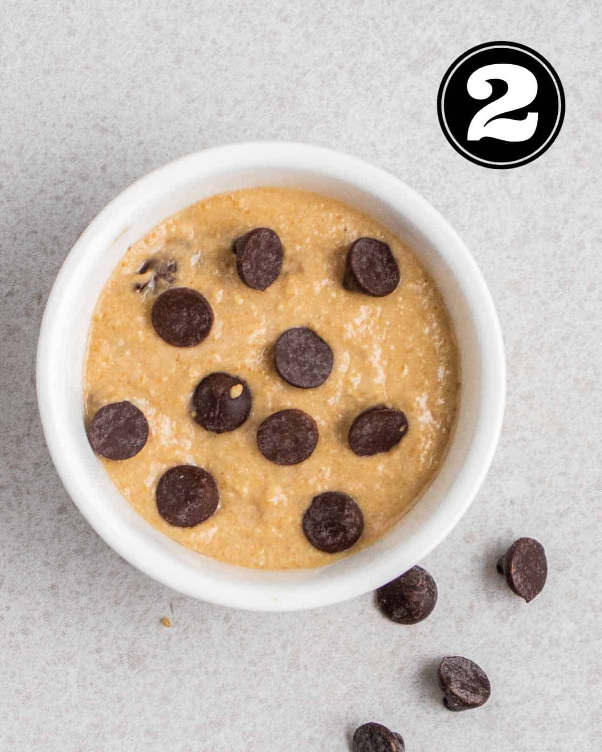 Mug cookie batter in a ramekin topped with chocolate chips.