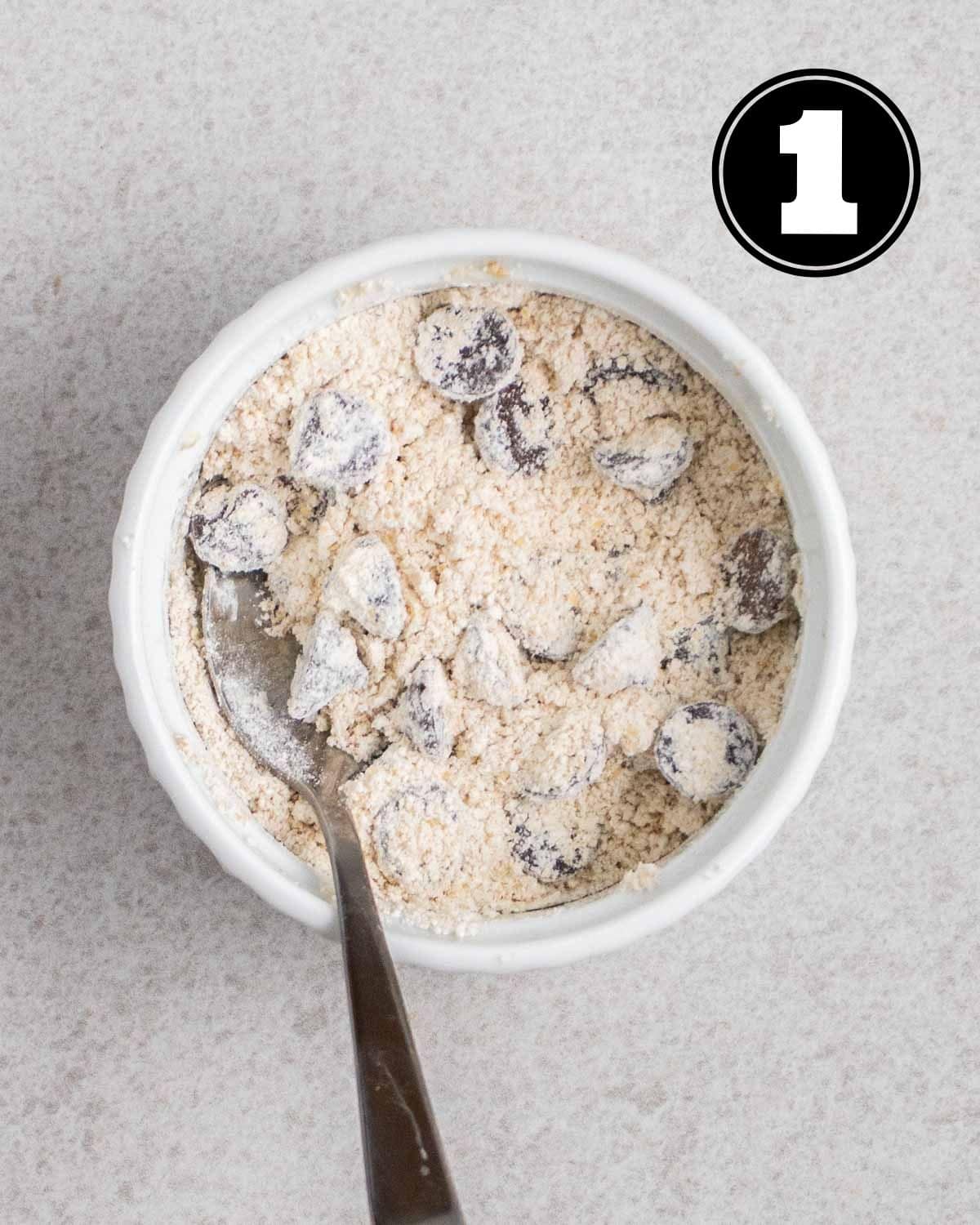 Dry ingredients for mug cookie in a ramekin with a teaspoon beside.