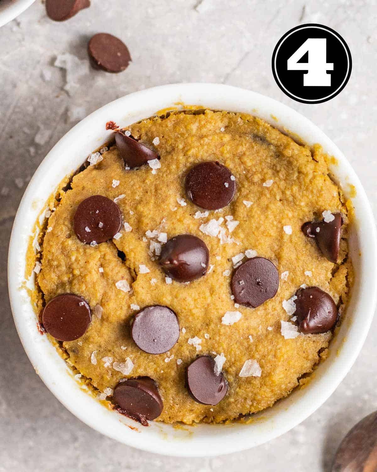 Mug cookie topped with flaky sea salt with a teaspoon beside.