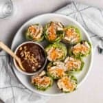 A plate of halved rice paper rolls served with peanut sauce.
