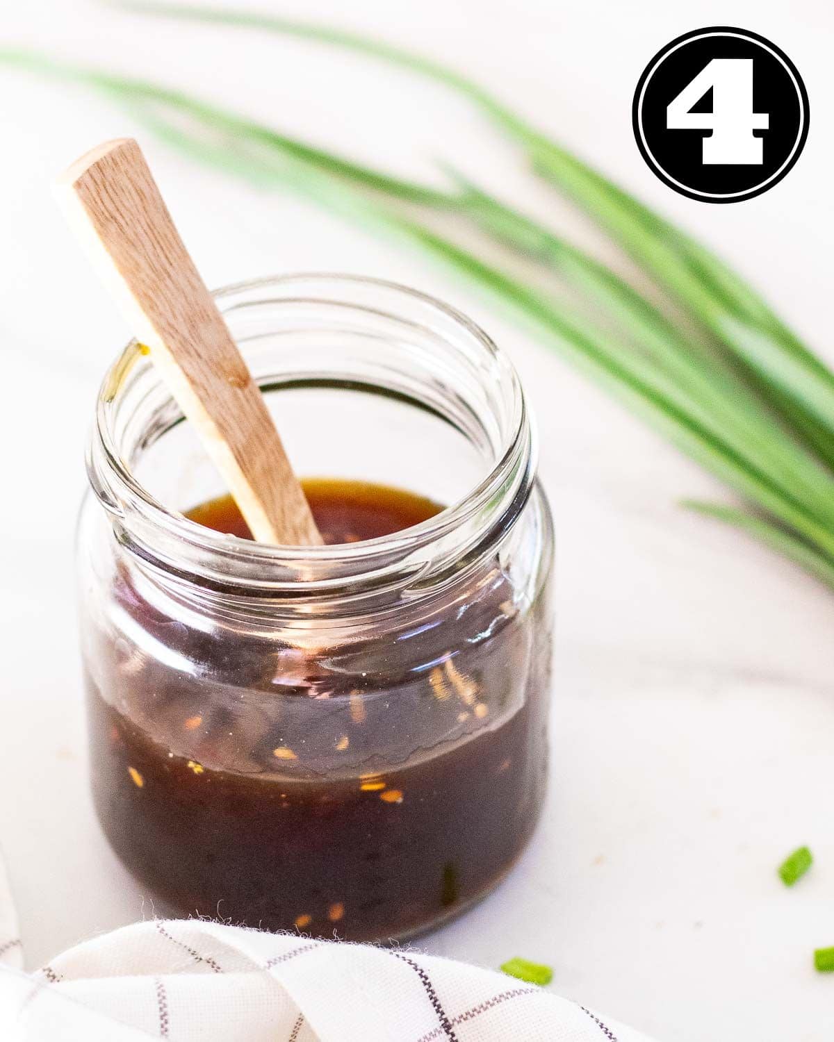 A jar of teriyaki sauce with a wooden spoon with a stalk of green onion in the background.