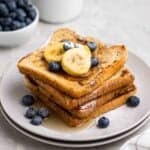 A stack of french toast topped with sliced bananas and blueberries.