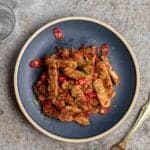 A plate of sambal tempeh with fork and glass of water beside.