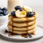 Stack of pancakes with maple syrup dripping over with blueberries and glass of milk in the background.