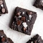 Slices of protein brownies topped with flakes sea salt arranged on a parchment paper.