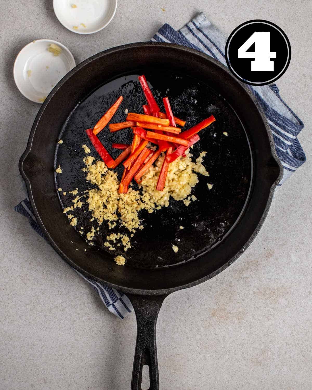 Cooked aromatics in a cast iron skillet with 2 sauce dishes beside.