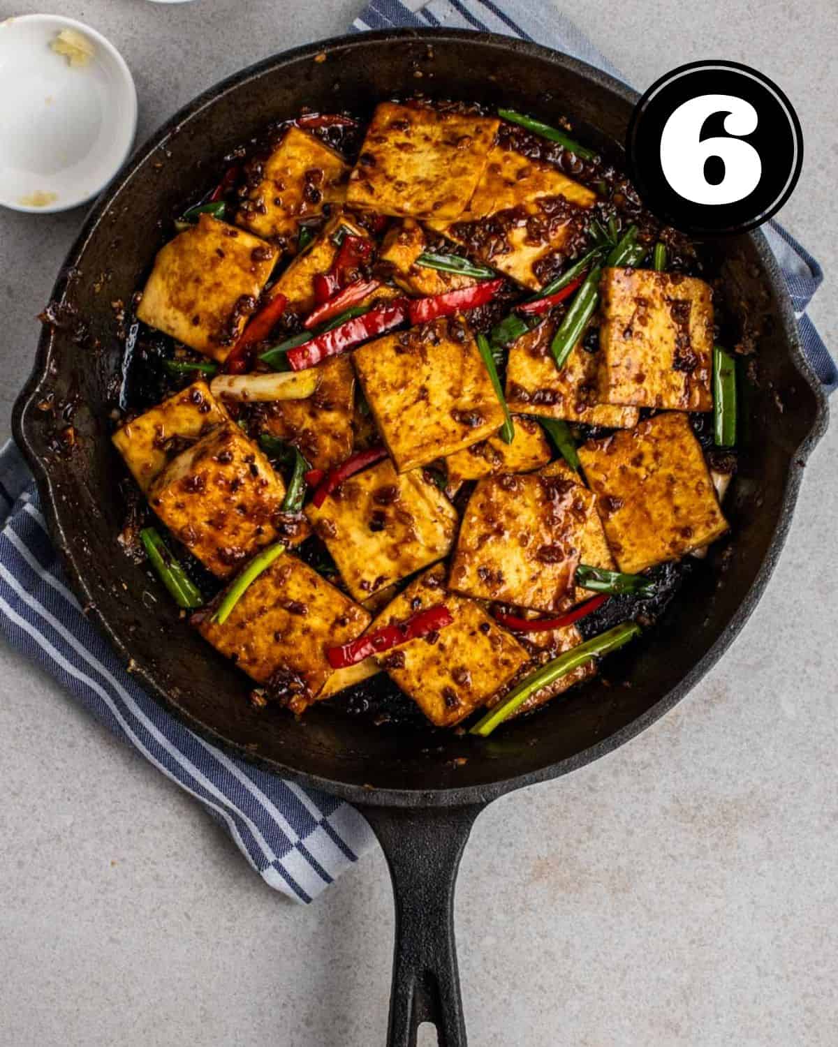Black bean sauce tofu in a cast iron skillet with 2 sauce dishes beside.