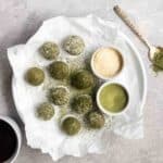 A plate of matcha balls with dish of dessicated coconut and matcha beside.