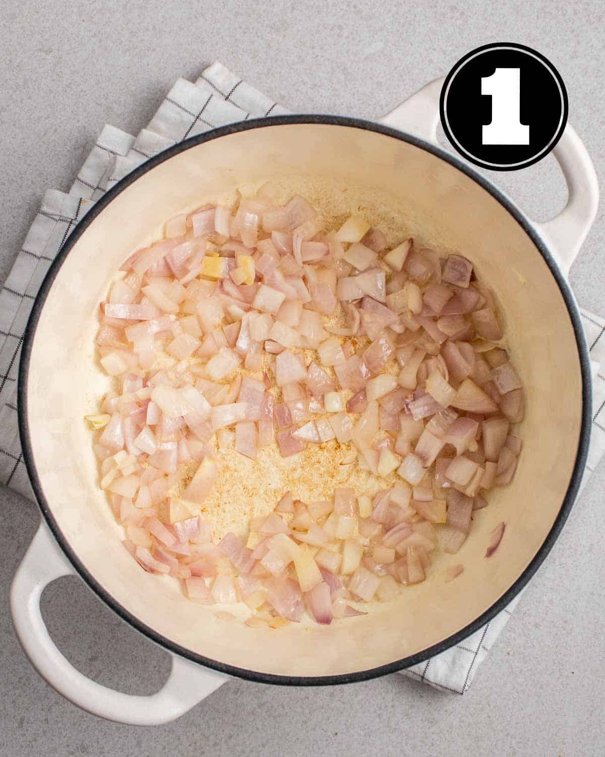 Cooked onion in a Dutch oven on a folded white checkered teacloth.