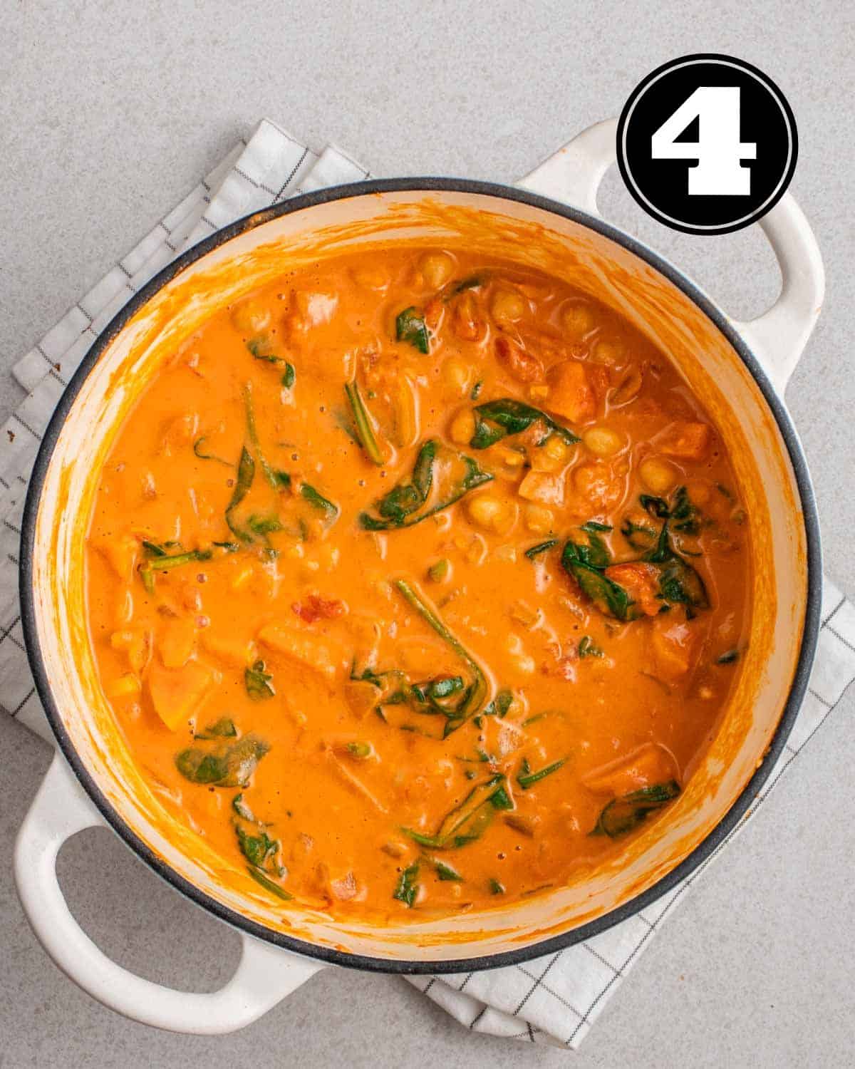 A pot of sweet potato chickpea spinach curry on a folded white teacloth.
