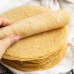 Rolling a piece of chickpea tortilla on a stack of tortillas.