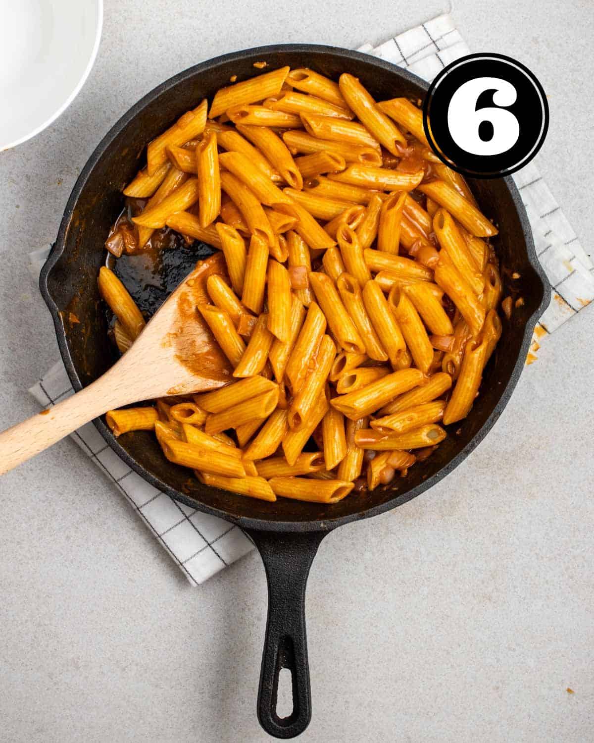 Cooked gochujang pasta in a cast iron skillet with a wooden spatula beside.