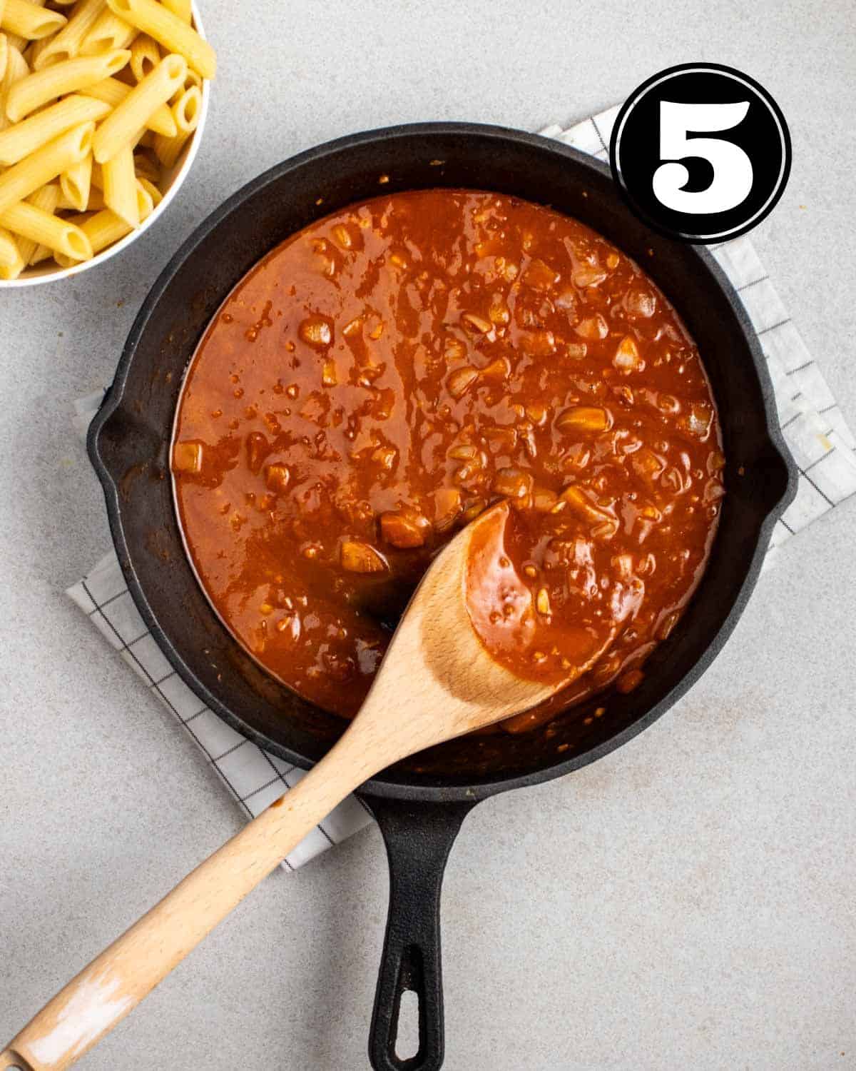 Simmering sauce in a cast iron skillet with a wooden spatula beside.