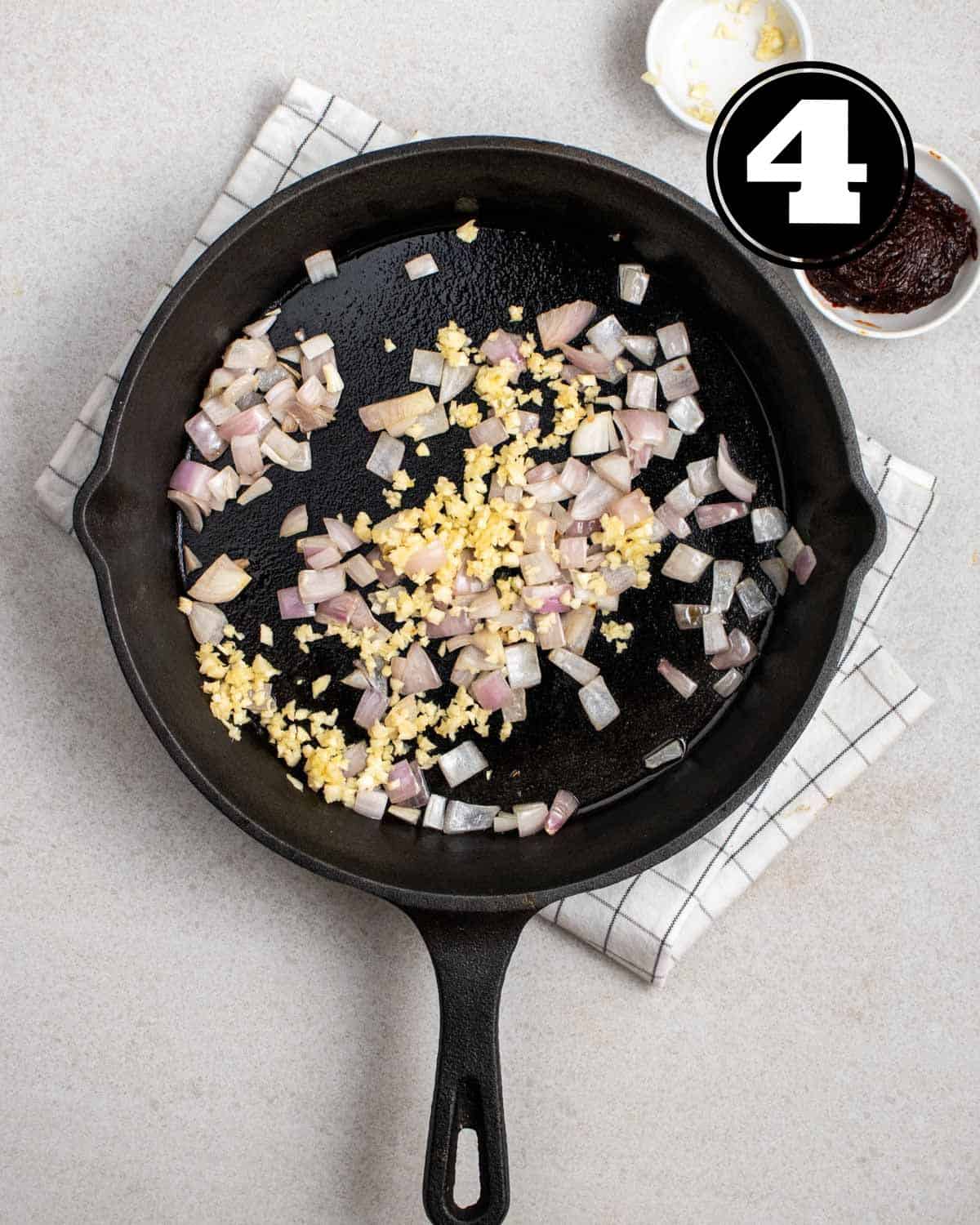Cooked garlic and onion in a cast iron skillet on a white folded teacloth.