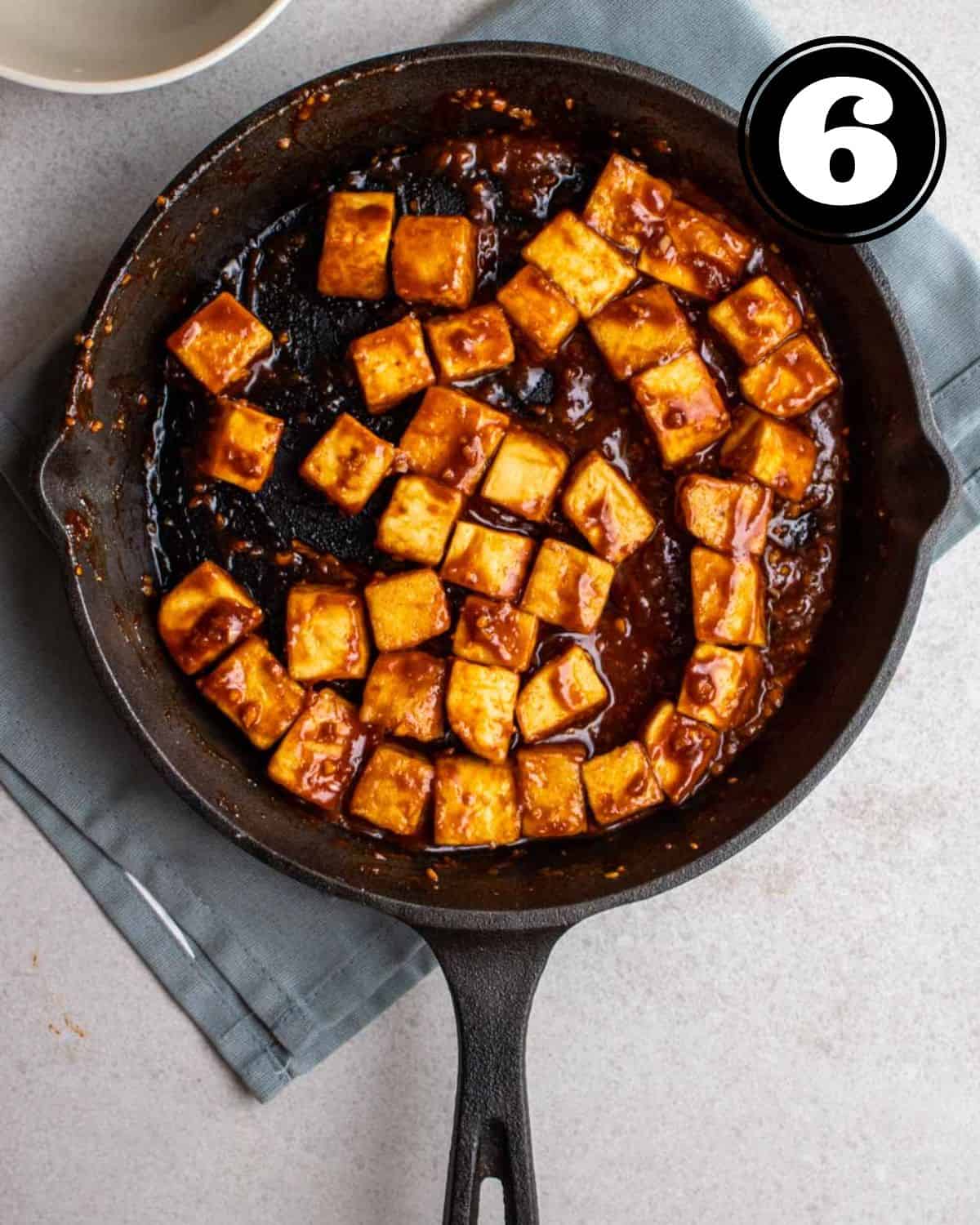 Gochujang tofu in a cast iron skillet on a blue folded teacolth.