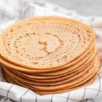 A stack of tortillas on a plate lined with a white checkered teacloth.
