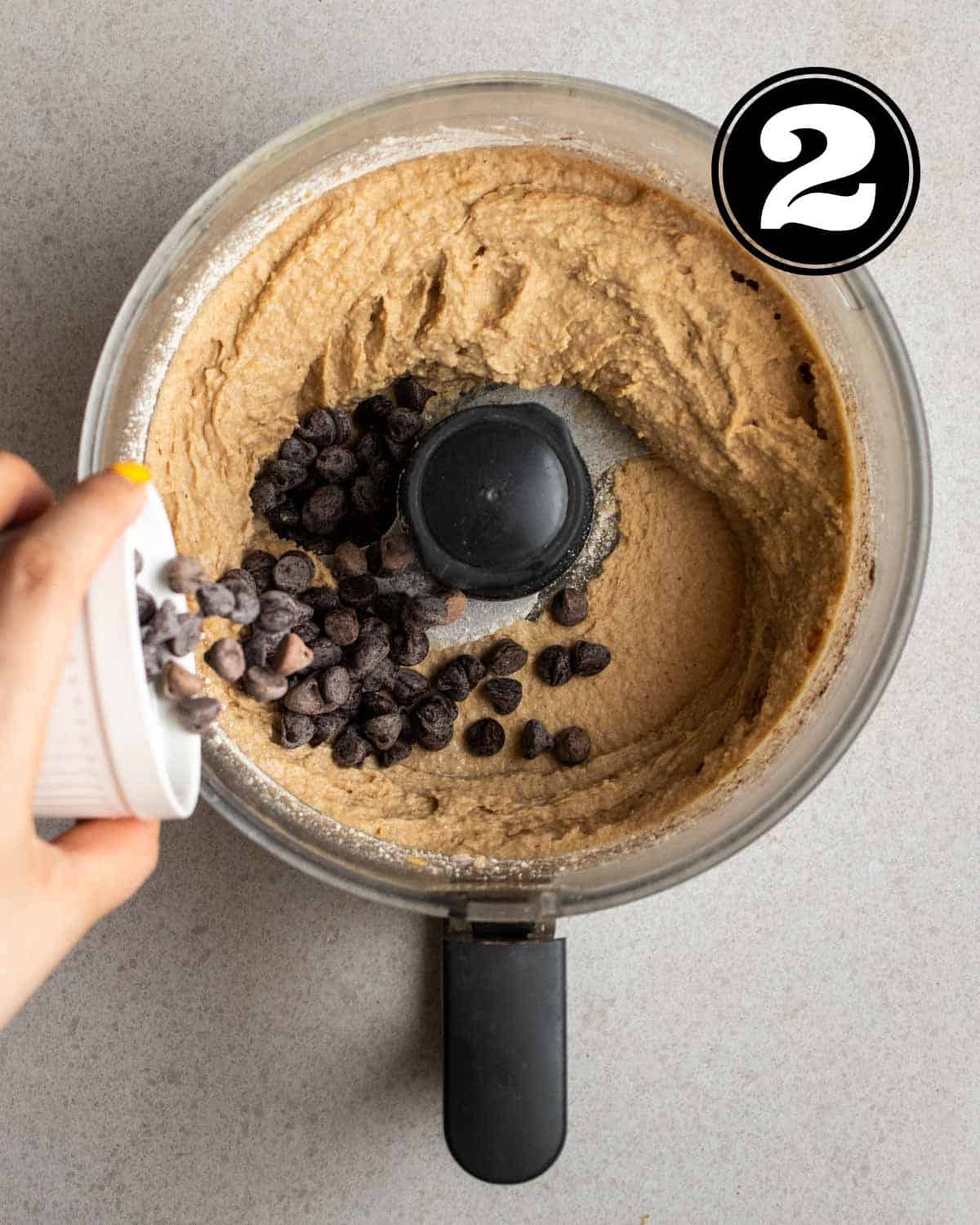 Adding chocolate chips into a food processor with cookie batter.
