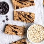 Protein bars arranged on a parchment paper with a bowl of chocolate chips and oats beside.