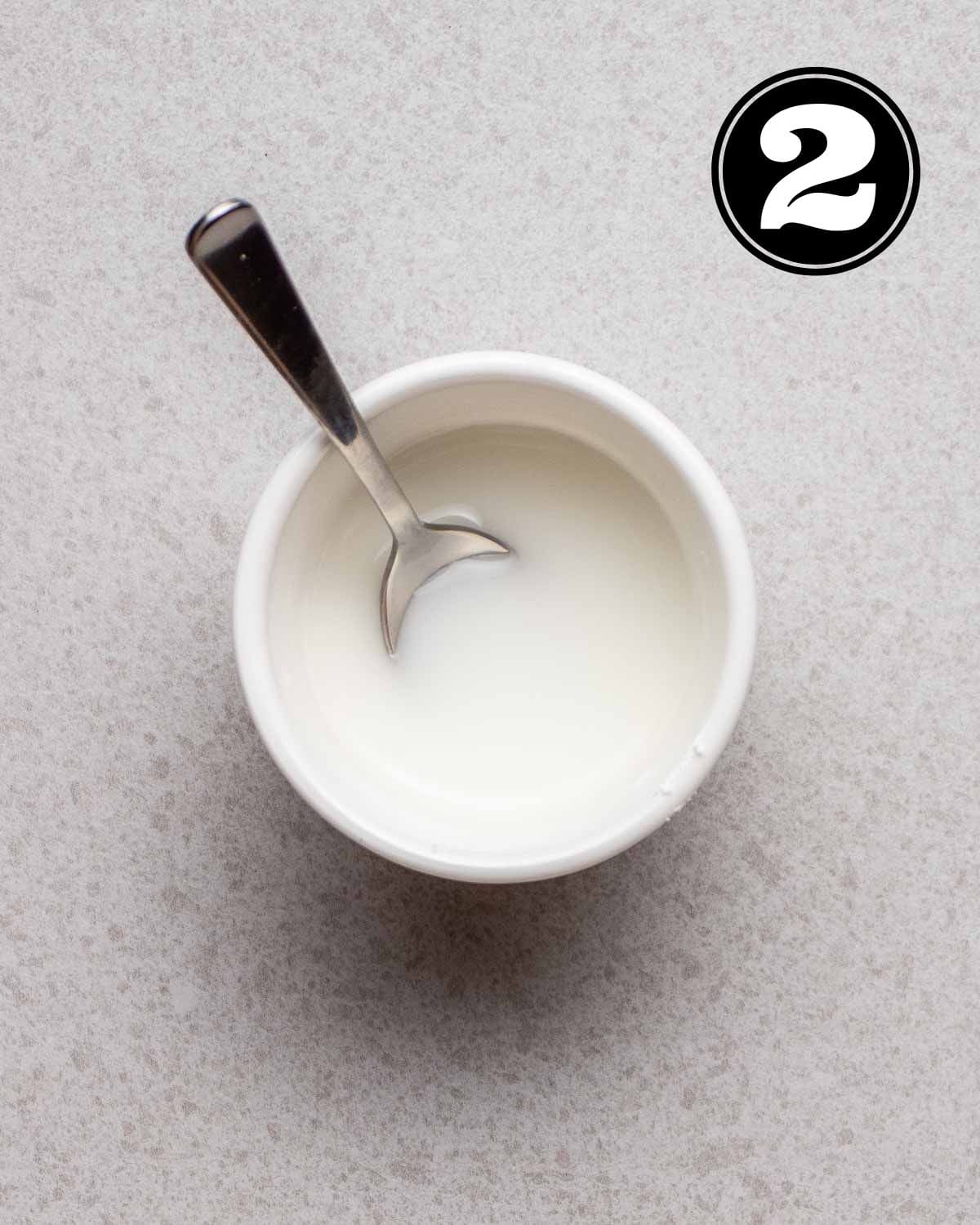 Cornstarch slurry in a white bowl with a teaspoon beside.